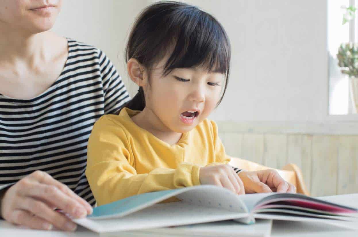 Young asian girl reads pointing a finger as she follows the words in a book