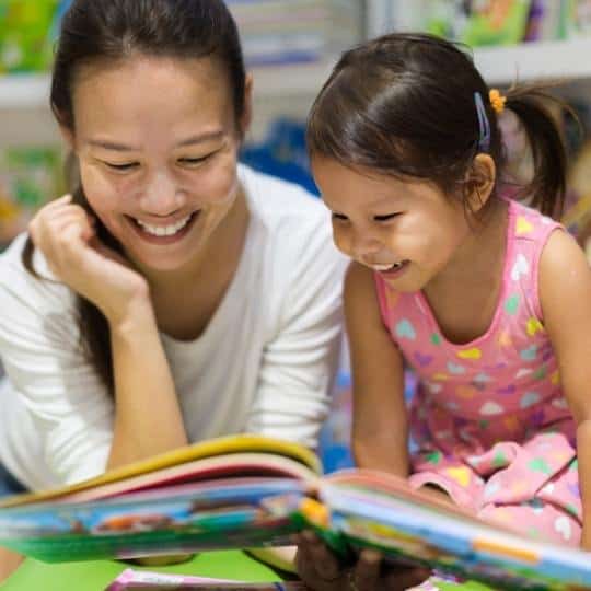 Woman and young girl smiling as they read a book together