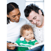 Smiling parents with book ope reading to curly haired toddler in a green top
